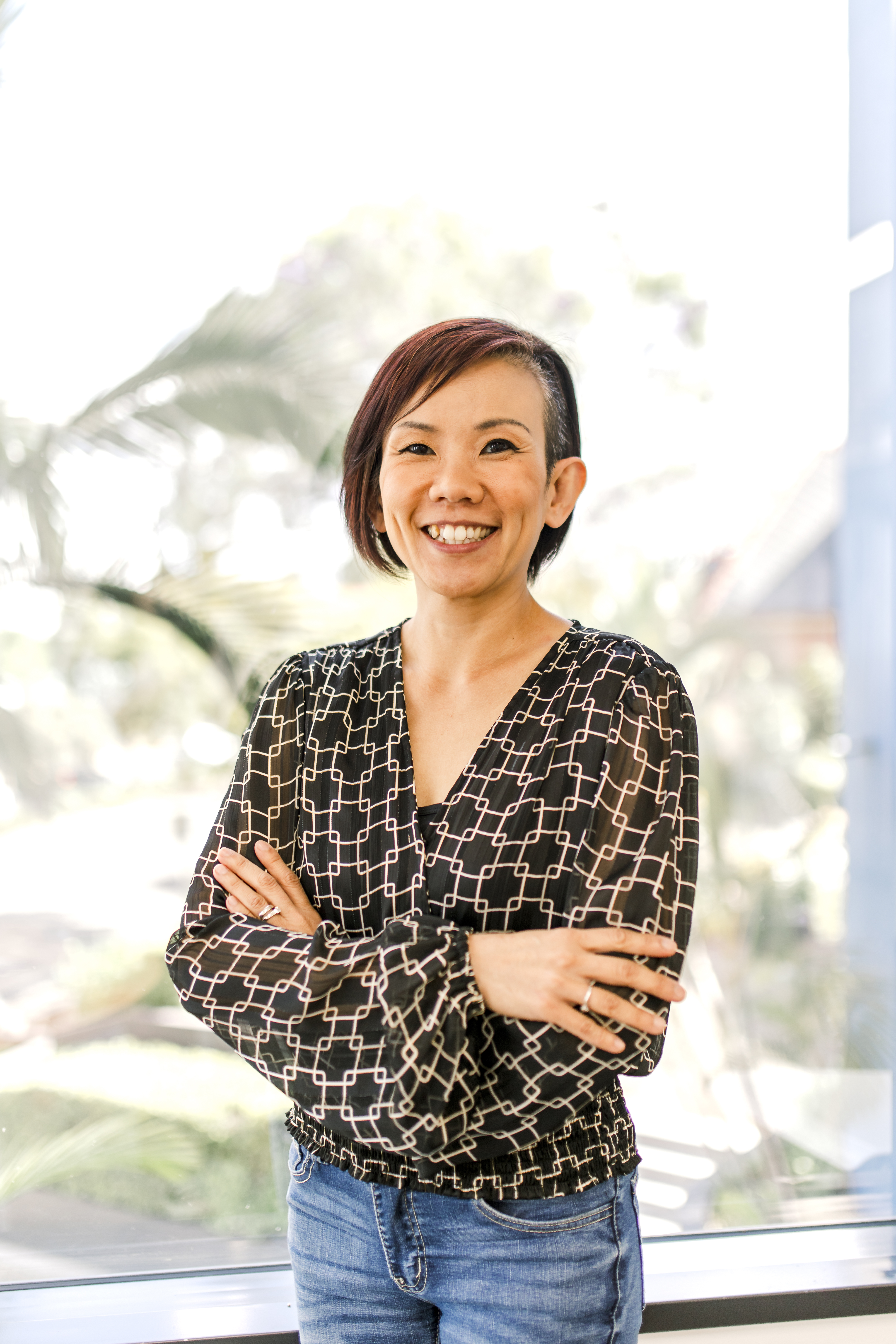 Alicent Wong standing with dark chin length hair, arms folding wearing jeans and black and tan pattern blouse